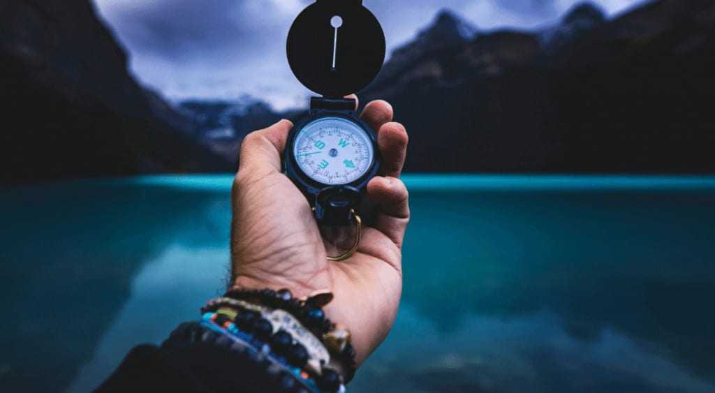 Man holds a compass by a lake