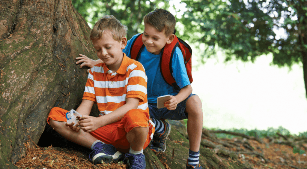 Two boys find a geocache under a tree